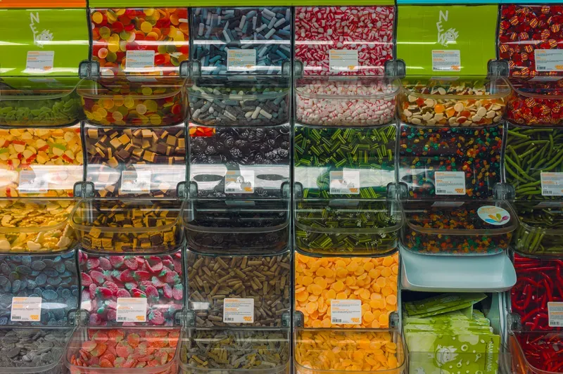 A wall of clear pick-and-mix bins packed with sweets in every colour, from pink and white striped to green sours and orange discs.