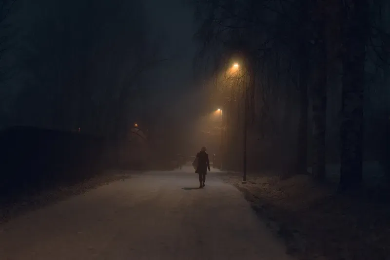 A figure recedes down a fog-filled street, lit only by the soft glow of streetlamps.