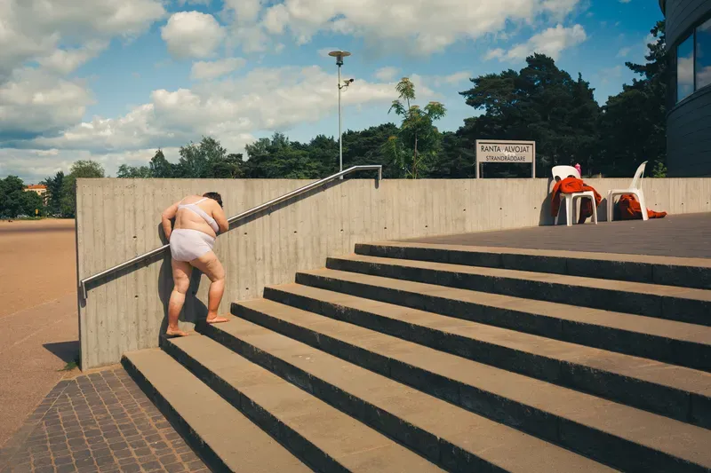 A shirtless child leaps down concrete steps mid-motion under a bright sky.