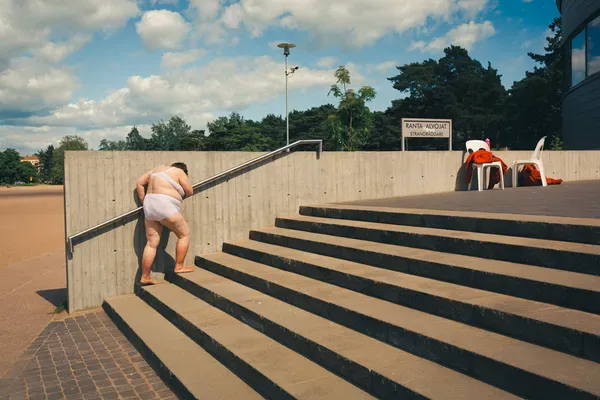 A shirtless child leaps down concrete steps mid-motion under a bright sky.