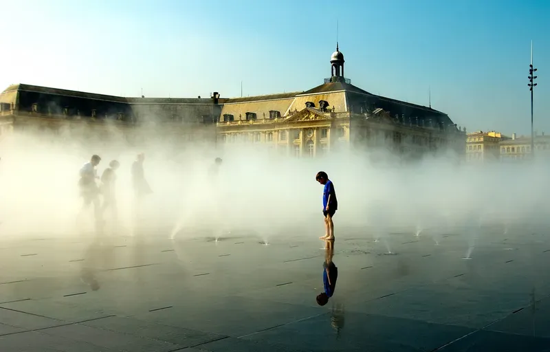Figures dissolve into fog on a mist-covered plaza, one reflected clearly in the wet stone underfoot.