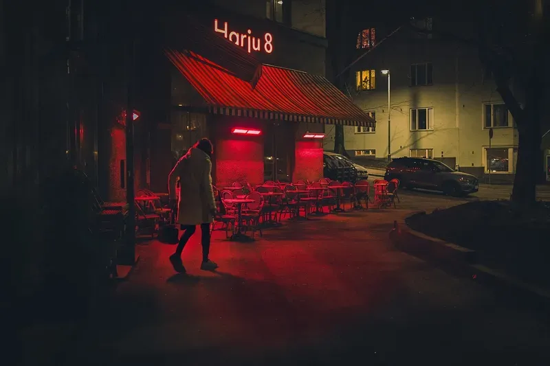 A woman walks past an outdoor café glowing red in the evening light.