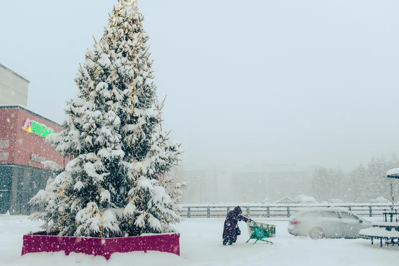 A snow-covered Christmas tree stands over a small figure playing in the snow below.