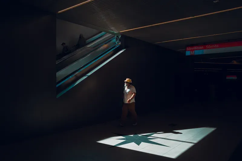 A man in a straw hat walks through a metro station past a pool of sunlight that lights up a compass star inlaid in the floor.