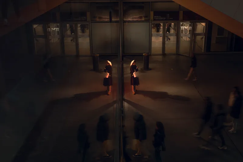 Two women are doubled in a mirrored corridor, their reflections multiplying as passersby blur in the background.
