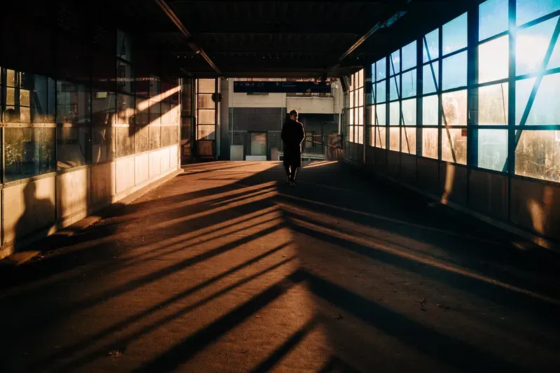 A man walks through a sunlit elevated walkway in Helsinki, long shadows cast by the structure's steel beams.